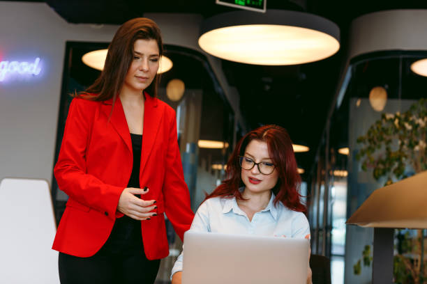 istock Strategic Collaboration: Two Young Business Women Utilizing Digital Tablet and Laptop in a Modern Startup Office. Planning, Strategizing, and Discussing Success as a Team in the Boardroom Meeting 1959850281