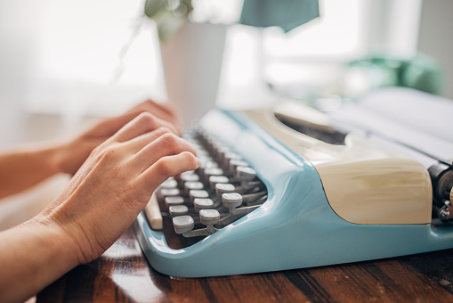 Unrecognizable young woman typing on a typewriter in her apartment.