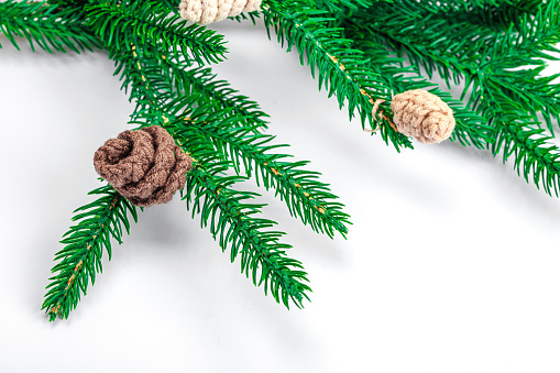 Cozy crocheted pine cones on evergreen Christmas tree branch. Creative handmade decor, craft mood concept. White background, winter flat lay, copy space
