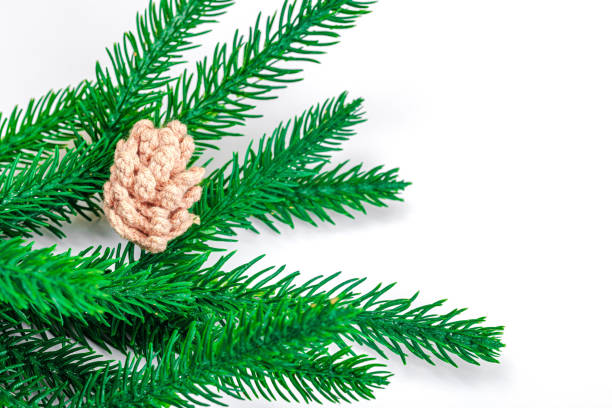 Cozy crocheted pine cones on evergreen Christmas tree branch. Creative handmade decor, craft mood concept. White background, winter flat lay, top view
