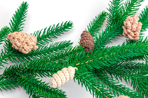 Cozy crocheted pine cones on evergreen Christmas tree branch. Creative handmade decor, craft mood concept. White background, winter flat lay, close up
