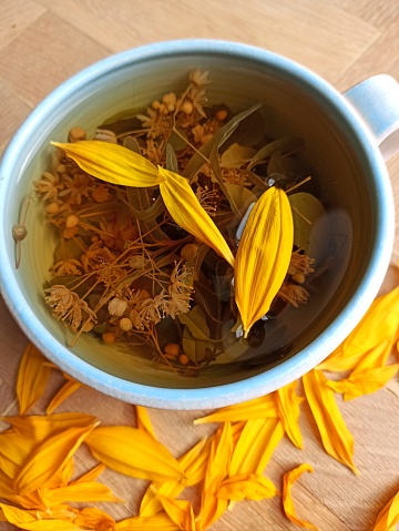 Cup of tea in a blue mug with linden and sunflower petals, herbal floral tea