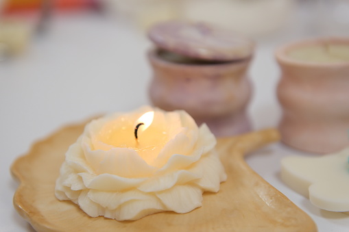 lit burning candle in form of a rose with wax petals against the background of massage candles spa salon interior beautifully burning fire relaxation pleasant time beauty self care. massage treatments