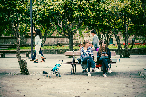 Pontevedra, Spain - September 24, 2016: Two young women, sitting on a bench, while one of them consults her smartphone.