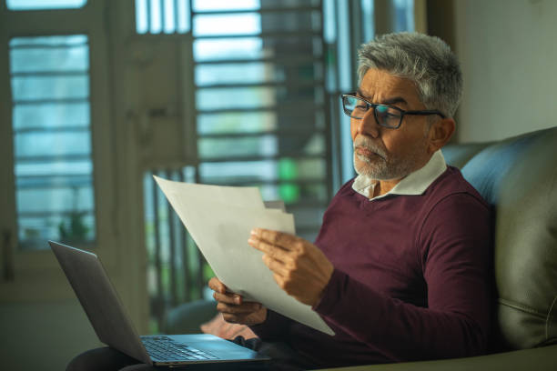 istock Old man with documents and laptop sitting on sofa 1959878904