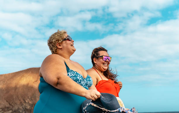 istock Happy plus size women having fun walking on the beach during summer vacations - Overweight people concept 1959884704