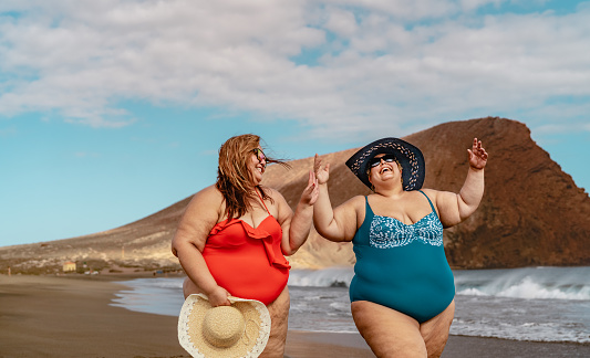 Happy plus size women having fun walking on the beach during summer vacations - Overweight people concept