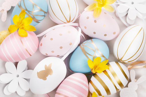 Colorful pink blue white golden Easter eggs and spring yellow flowers background. Happy Easter concept