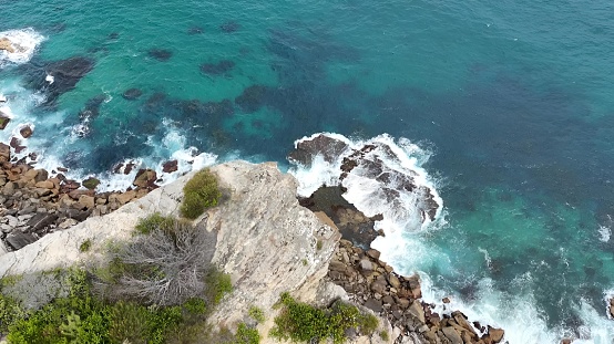 A stunning aerial view of a rugged coastal landscape featuring jagged cliffs and crystal clear blue-green ocean waters in the background