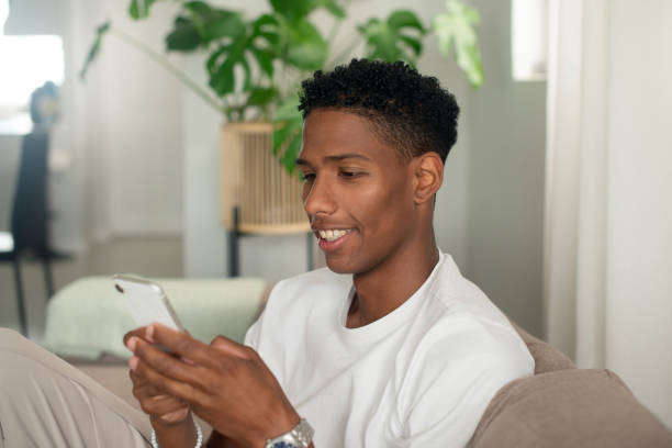 istock Young man, text message or positive on couch for notification or social media to relax on weekend in home. Student, smile and cellphone in connection with online games, wellness and vacation on sofa 1959919845