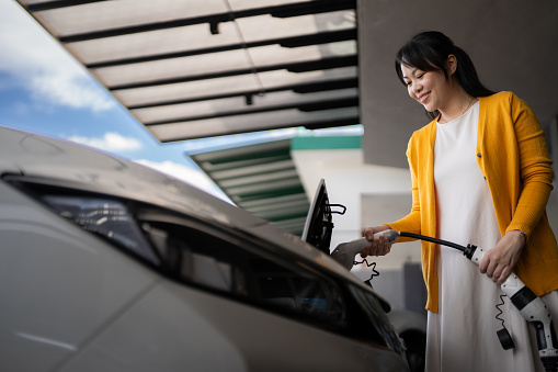 Adult woman plugging in an electric car at home