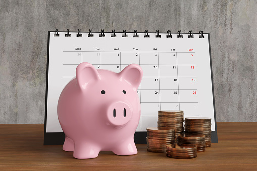 Pink piggy bank, desk calendar and stacks of gold coins on a wooden table. Illustration of the concept of financial planning and retirement preparation