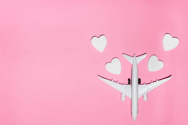 istock Valentine's Day is travel concept. White passenger plane with hearts on pink background. Flat lay vacation planing and traveling holiday. Top view 1959964630