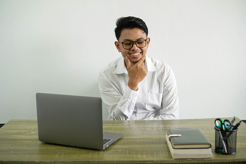 young asian businessman in a workplace smiling looking to the side, wearing white shirt with glasses isolated