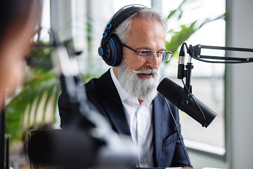 A live corporate podcast captures a senior Caucasian host with a gray beard in a deep discussion with a Black mid adult female guest in a modern office setting.