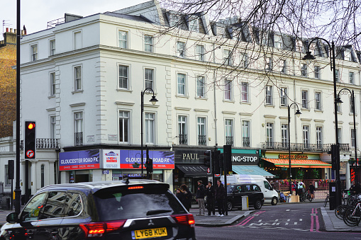 Cromwell Road, The Royal Borough of Kensington and Chelsea, London, England, United Kingdom, Britain — 24 January 2024: In the winter daylight, a view of a west London street unfolds, positioned on the west side of Central London within The Royal Borough of Kensington and Chelsea's upper-class district. Renowned for its exclusive real estate, this scene captures a typical urban perspective from West London, featuring some cars halted at a red light, adding a touch of daily life to the prestigious Kensington atmosphere.