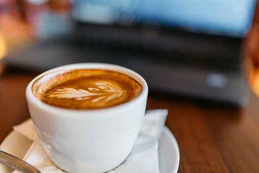 Cup of coffee and a laptop on the table in a coffee shop.