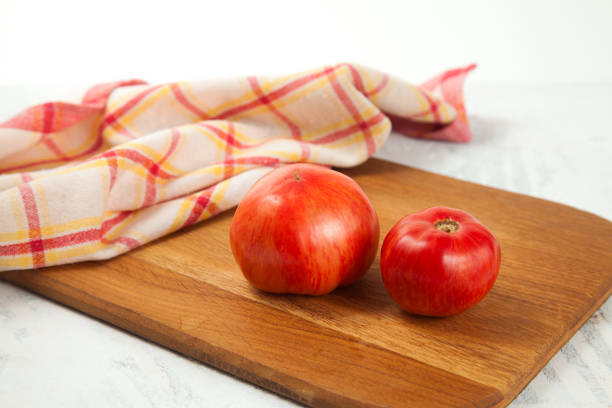istock Cutting board with several pink tomatoes and red kitchen towel on white wooden background. 1960101815