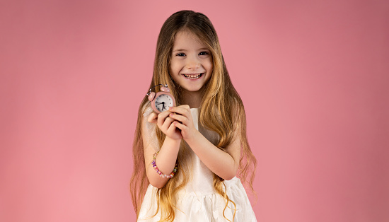 Portrait of a very beautiful and special little girl with very arranged and attractive hair, she is happy and holding a pink clock in her hand. Fetitza is very cute with this watch in her hand. High quality photo