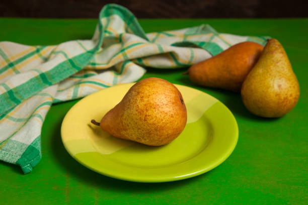 Green plate with ripe juicy pear fruit and green kitchen towel on green wooden background.