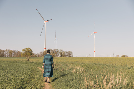 Woman in blue dress walking along a small road towards wind turbine fields outside Brandenburg germany