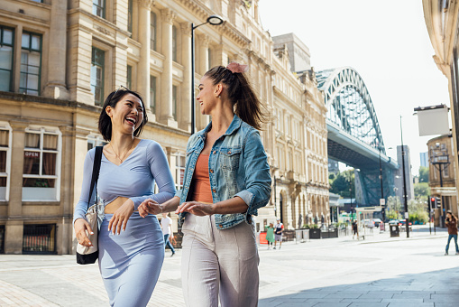 Two women wearing fashionable, casual clothing, walking through Newcastle City Centre, England. They are talking, smiling and laughing together as they walk.