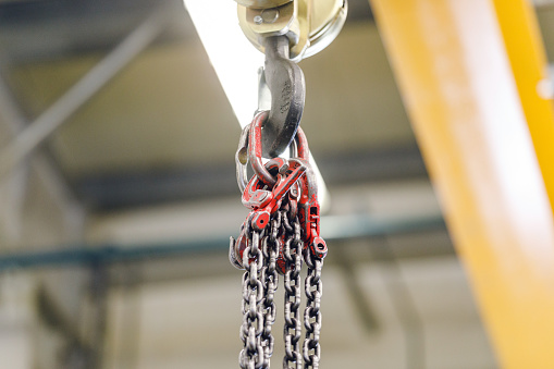 Metallic industrial hook meant for lifting heavy things in a factory. The hook has chains on it.