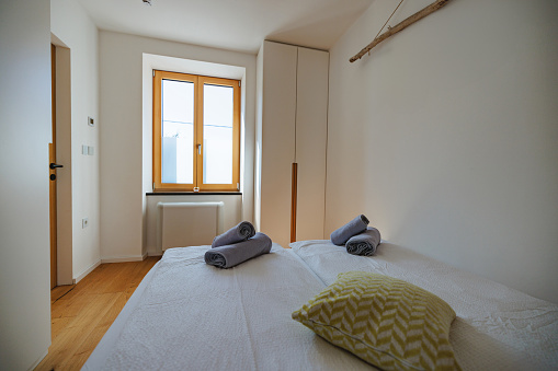 A rear photo of a nice and cozy bed with white sheets and a cushion ready to receive their firsts guests at an apartment for rent. There is a window at the back that illuminates all the room with natural daylight.
