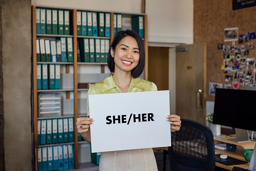 A portrait of a beautiful businesswoman standing in an office interior in Newcastle, England. She has a confident expression and she's looking at the camera with a smile while holding a sign which reads \