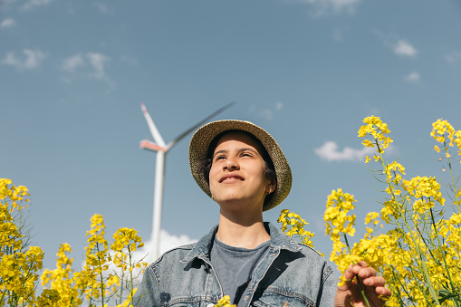 Portrait of girl with hat and denim jacket smiling in a field of yellow flowers next to windmills