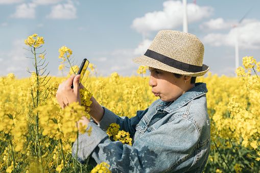 Girl with hat making photo of yellow flowers with mobile phone