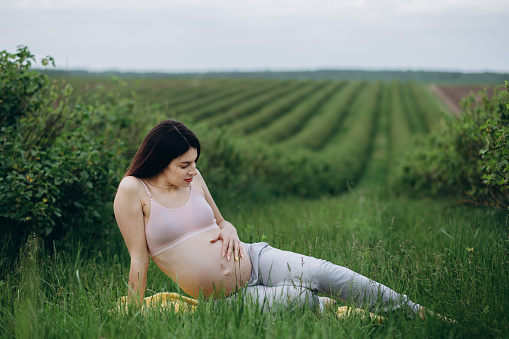 Happy young pregnant woman sitting on grass doing yoga in summer day