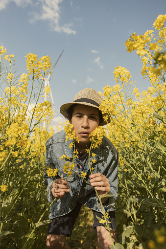 Teenage girl in a denim jacket smiling in a field of yellow flowers next to a windmill field