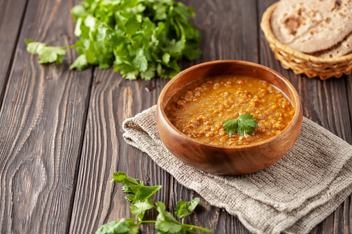 Indian dal food (Masoor Dal or Dal Tadka Curry) and homemade Flatbread Chapati. Traditional Indian soup lentils. Indian Dhal spicy curry in bowl, spices, herbs, rustic black wooden background.