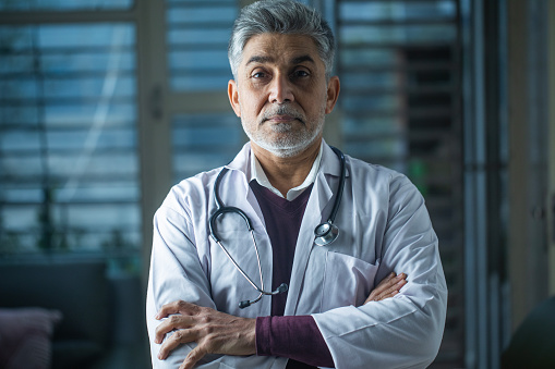 Portrait of confident senior male doctor dressed in lab coat while standing in hospital