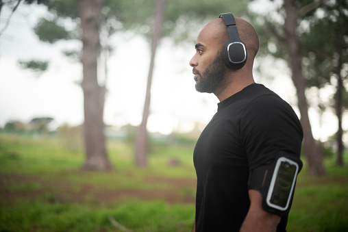 Man in headphones, forest and thinking of fitness, workout or running goals, journey and listening to health audio. Sports person or runner with music on mobile for exercise or training in nature