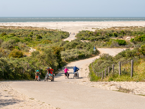 People walking with bicycles climbing steep hill of Duinhoevepad in dunes near Renesse on Schouwen-Duiveland, Zeeland, Netherlands