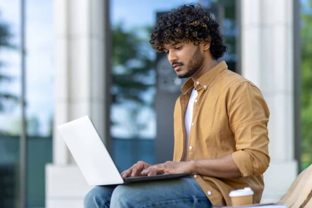 istock Concentrated and serious young Indian man using a laptop while sitting on a bench outside 1960208457