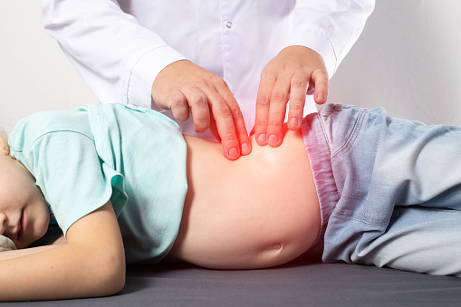 A doctor surgeon examines and diagnoses the abdomen of a seven-year-old little girl who has abdominal pain. Concept of appendicitis in children, nausea and discomfort, inflammation