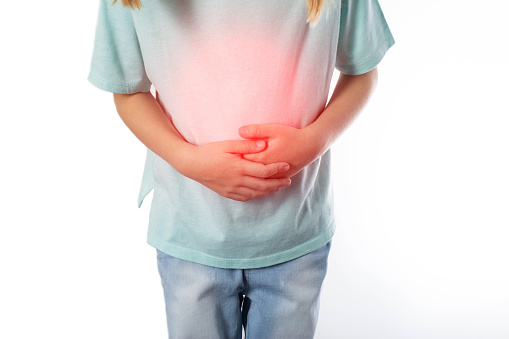 A seven-year-old girl in a green T-shirt holds her inflamed red stomach with her hands on a white background, isolate. Disease concept with colic and abdominal cramps, appendicitis in children.