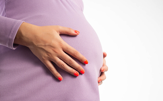 Female hands with manicure on a woman's pregnant belly. The concept of nail care, the benefits and harms of gel nail polish during pregnancy. Copy space for text, hormones