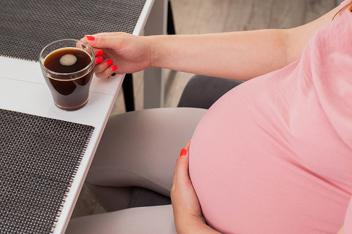 Pregnant girl drinks coffee from a cup. The benefits and harms of coffee for pregnant women.