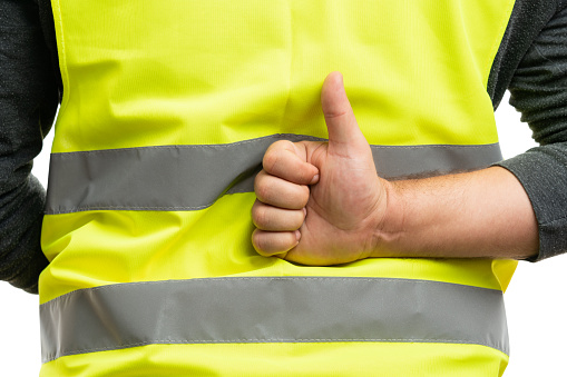 Close-up of like agree thumb-up gesture made by adult builder man behind back wearing fluorescent vest isolated on white background