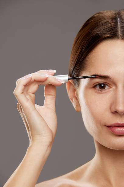 istock Poster for beauty workshop teaching professional makeup application. Woman holding brow fixing gel against studio background 1960235949