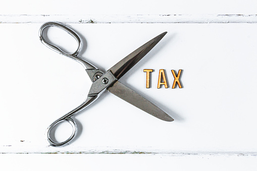 Cutting taxes concept illustrated with wooden letters spelling the word 'tax' with scissors.