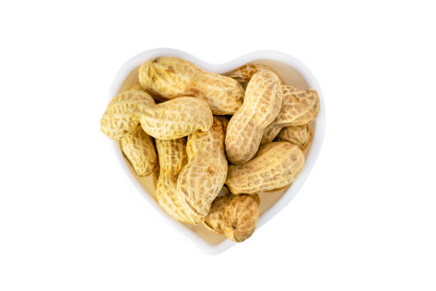 Peanuts in shell in a heart shaped cup, delicious groundnut isolated on white background. Nuts close-up. Healthy natural snack.