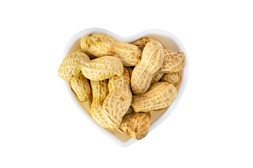 Top view of a bunch of dried peanuts in shell in a heart shaped cup, delicious groundnut isolated on white background. Nuts close-up. Healthy natural snack.