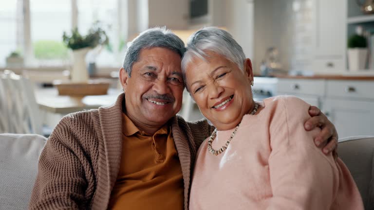 Senior couple, face and hug on couch, smile and bonding with love, support and relax in retirement in home. Elderly woman, old man and portrait with embrace, together and sitting on living room sofa