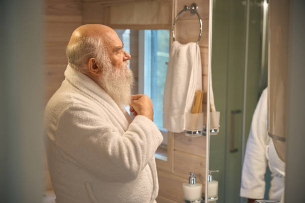 istock Old man in bathroom in front of mirror combs his beard 1960241796