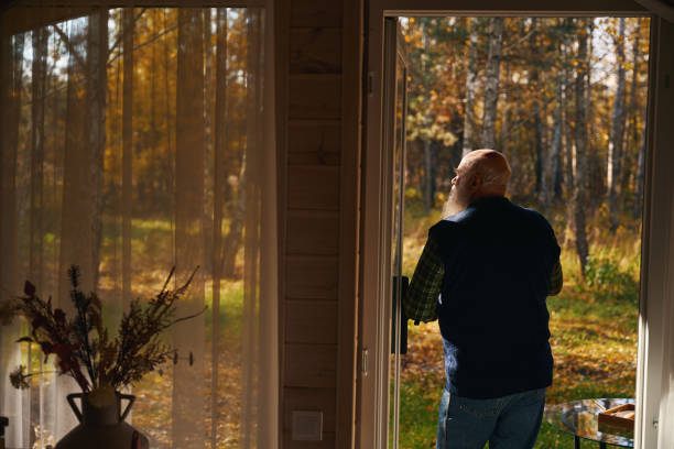 Gray-bearded man admires the autumn forest, he stands on the veranda of a country house